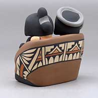 A grandparent storyteller figure, wearing a manta and holding four children with gifts, click or tap to see a larger version