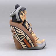 A grandparent storyteller figure, wearing a manta and holding four children with gifts, click or tap to see a larger version