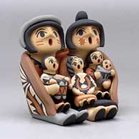 A grandparent storyteller figure, wearing a manta and holding four children with gifts, click or tap to see a larger version