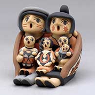A grandparent storyteller figure, wearing a manta and holding four children with gifts
 by Chrislyn Fragua of Jemez