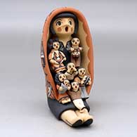 A sitting grandmother storyteller wearing a manta and holding seven children and gifts
 by Chrislyn Fragua of Jemez