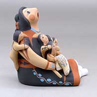 A sitting grandmother storyteller with five children, a folded manta and a welcome basket, click or tap to see a larger version