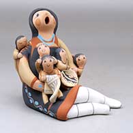 A sitting grandmother storyteller with five children, a folded manta and a welcome basket, click or tap to see a larger version