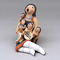 A sitting grandmother storyteller with five children, a folded manta and a welcome basket
 by Diane Lucero of Jemez