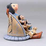 A sitting grandmother storyteller wearing a manta and skirt with four children, a puppy and a drum, click or tap to see a larger version