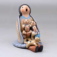 A sitting grandmother storyteller wearing a manta and skirt with four children, a puppy and a drum, click or tap to see a larger version