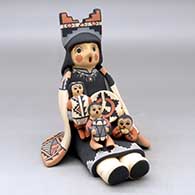 A grandmother storyteller figure wearing a manta and a tablito and holding three children with gifts and a welcome basket
 by Linda Lucero Fragua of Jemez