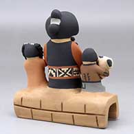 A grandmother storyteller figure sitting on a stone wall with four children, a puppy and a welcome basket, click or tap to see a larger version