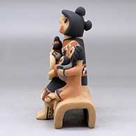 A grandmother storyteller figure sitting on a stone wall with four children, a puppy and a welcome basket, click or tap to see a larger version