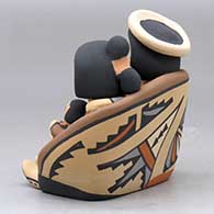 A grandparent storyteller figure sitting on a stone wall with six children, click or tap to see a larger version