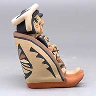 A grandparent storyteller figure sitting on a stone wall with six children, click or tap to see a larger version