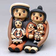 A grandparent storyteller figure sitting on a stone wall with six children
 by Chrislyn Fragua of Jemez