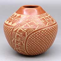 A red jar decorated with a four panel sgraffito snowflake, kiva step, spiral and geometric design
 by Wilma Baca Tosa of Jemez
