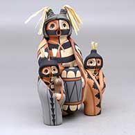 A koshare storyteller drummer with two children, all wearing mantas
 by Linda Lucero Fragua of Jemez