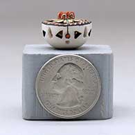 A miniature polychrome flat-topped jar decorated with a notched rim, cutouts and a flower and geometric design, click or tap to see a larger version