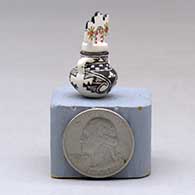 A miniature black on white jar with handles and a polychrome tablito lid and and decorated with a fineline, checkerboard and geometric design, click or tap to see a larger version