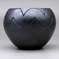 A micaceous black jar decorated with a lightly-carved avanyu, bear paw and geometric design, click or tap to see a larger version