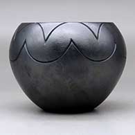 A micaceous black jar decorated with a lightly-carved avanyu, bear paw and geometric design, click or tap to see a larger version