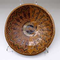 A large, shallow, polychrome bowl decorated with a shield, feather, yei and geometric design inside and a Navajo carpet pattern design outside
 by Nancy Yazzie of Dineh