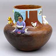 A Navajo Lifestyle pot with a sitting woman reading, dog and sheep appliques and a Monument Valley background
 by Elizabeth Manygoats of Dineh