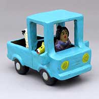 A woman driving a polychrome pickup with a dog in the seat and a sheep in the back
 by Elizabeth Manygoats of Dineh