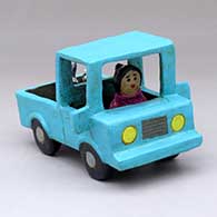 A woman driving a polychrome pickup with a dog in the back
 by Elizabeth Manygoats of Dineh