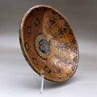 A shallow polychrome bowl decorated with a sgraffito and painted yeibichai, sun shield, feather and geometric design, click or tap to see a larger version