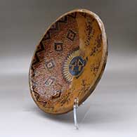 A shallow polychrome bowl decorated with a sgraffito and painted yeibichai, sun shield, feather and geometric design, click or tap to see a larger version