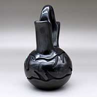 A black wedding vase carved with an avanyu and geometric design with an inlaid stone for its eye, click or tap to see a larger version