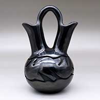 A black wedding vase carved with an avanyu and geometric design with an inlaid stone for its eye, click or tap to see a larger version