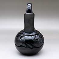 A black wedding vase carved with an avanyu and geometric design with an inlaid stone for its eye, click or tap to see a larger version