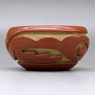 A red bowl decorated with a stylized avanyu design carved around the body, click or tap to see a larger version