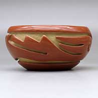 A red bowl decorated with a stylized avanyu design carved around the body, click or tap to see a larger version