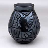 A matte and polished black jar decorated with a four-panel carved spiral, dragonfly, hummingbird and geometric design
 by Harrison Begay Jr of Santa Clara