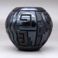 A matte and polished black jar decorated with a four-panel carved spiral, bear, feather and geometric design, click or tap to see a larger version