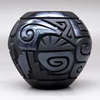 A matte and polished black jar decorated with a four-panel carved spiral, bear, feather and geometric design, click or tap to see a larger version