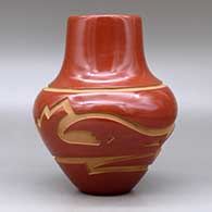 A red jar decorated with a carved avanyu and geometric design around the shoulder, click or tap to see a larger version