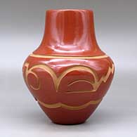 A red jar decorated with a carved avanyu and geometric design around the shoulder, click or tap to see a larger version