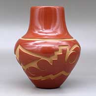 A red jar decorated with a carved avanyu and geometric design around the shoulder, click or tap to see a larger version