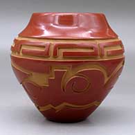 A red jar carved with an avanyu and geometric design around the body, click or tap to see a larger version