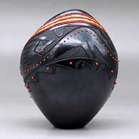 A black jar with an organic opening and decorated with a sgraffito avanyu and geometric design and bands of inlaid beads and stones, click or tap to see a larger version