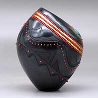 A black jar with an organic opening and decorated with a sgraffito avanyu and geometric design and bands of inlaid beads and stones, click or tap to see a larger version