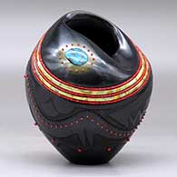 A black jar with an organic opening and decorated with a sgraffito avanyu and geometric design and bands of inlaid beads and stones, click or tap to see a larger version