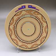 A polychrome plate decorated with a lightly carved and sgraffito avanyu, feather and geometric design with inlaid stones and strands of heishi beads
 by John Gonzales of San Ildefonso