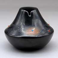A small black jar with sienna spots, several inlaid stones and decorated above the shoulder with a sgraffito avanyu and geometric design
 by Barbara Gonzales of San Ildefonso