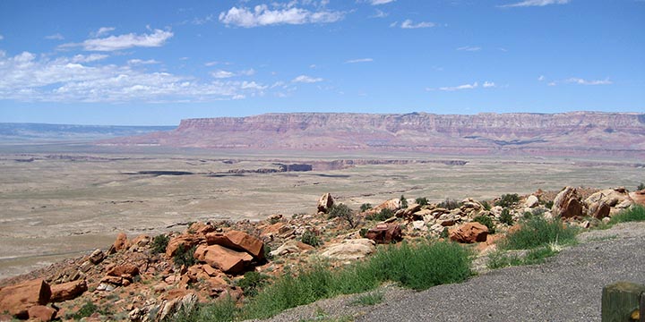 A view off the edge of Third Mesa near Old Oraibi with a flat green tableland below that is cut by a deeper canyon