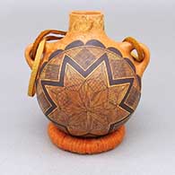 A black-on-red marbleized clay canteen decorated with a fine line and geometric design and a leather strap detail