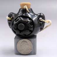 A miniature black canteen with handles and carved with an avanyu design on the front and rear
